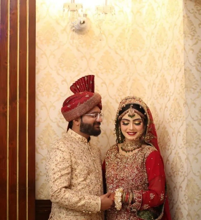 Groom in traditional sherwani and turban smiling with his bride